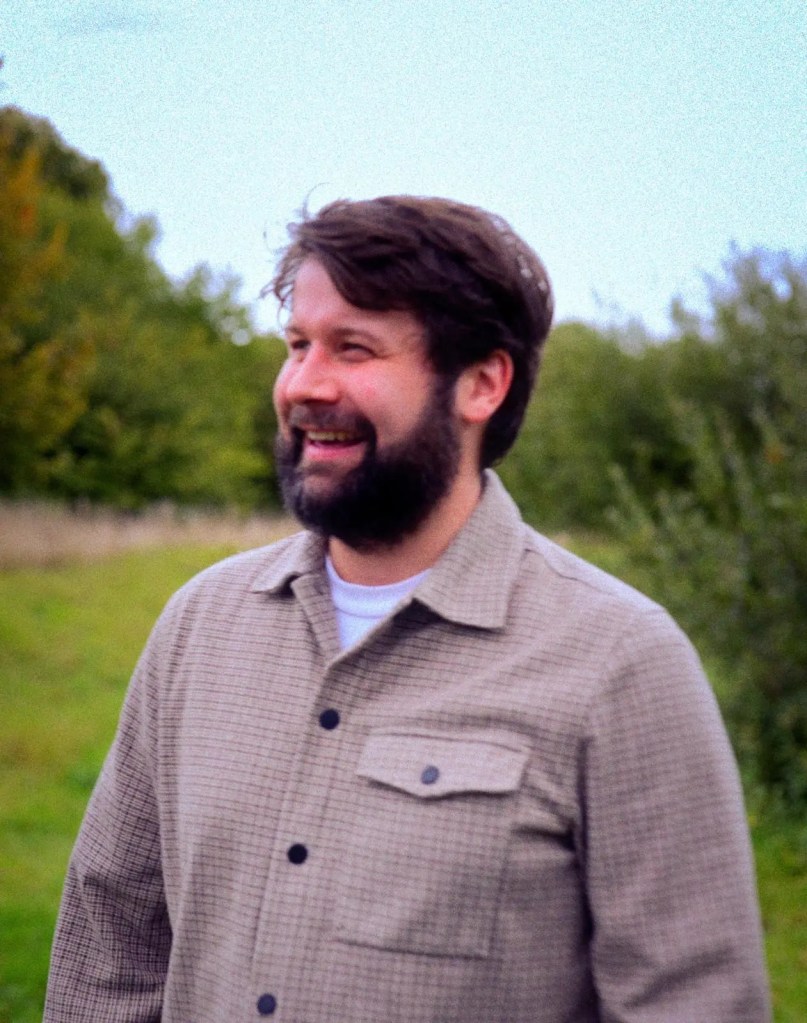 Man, Music, Musician, Artist, Pop, Song, Christmas, Dad, Newborn, Son, Love, Warm, Heartfelt, Hearty, Festive, Joyful, Grey, Shirt, Beard, Grass, Garden, Trees, Green, Sky, Cloud, Blue