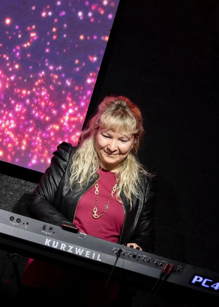 Woman, Divine, Religious, Worship, Catholic, Christian, Performing, Concert, Piano, Keys, Keyboard, Maroon, Tshirt, Jacket, Leather, Blonde, Kurzweil